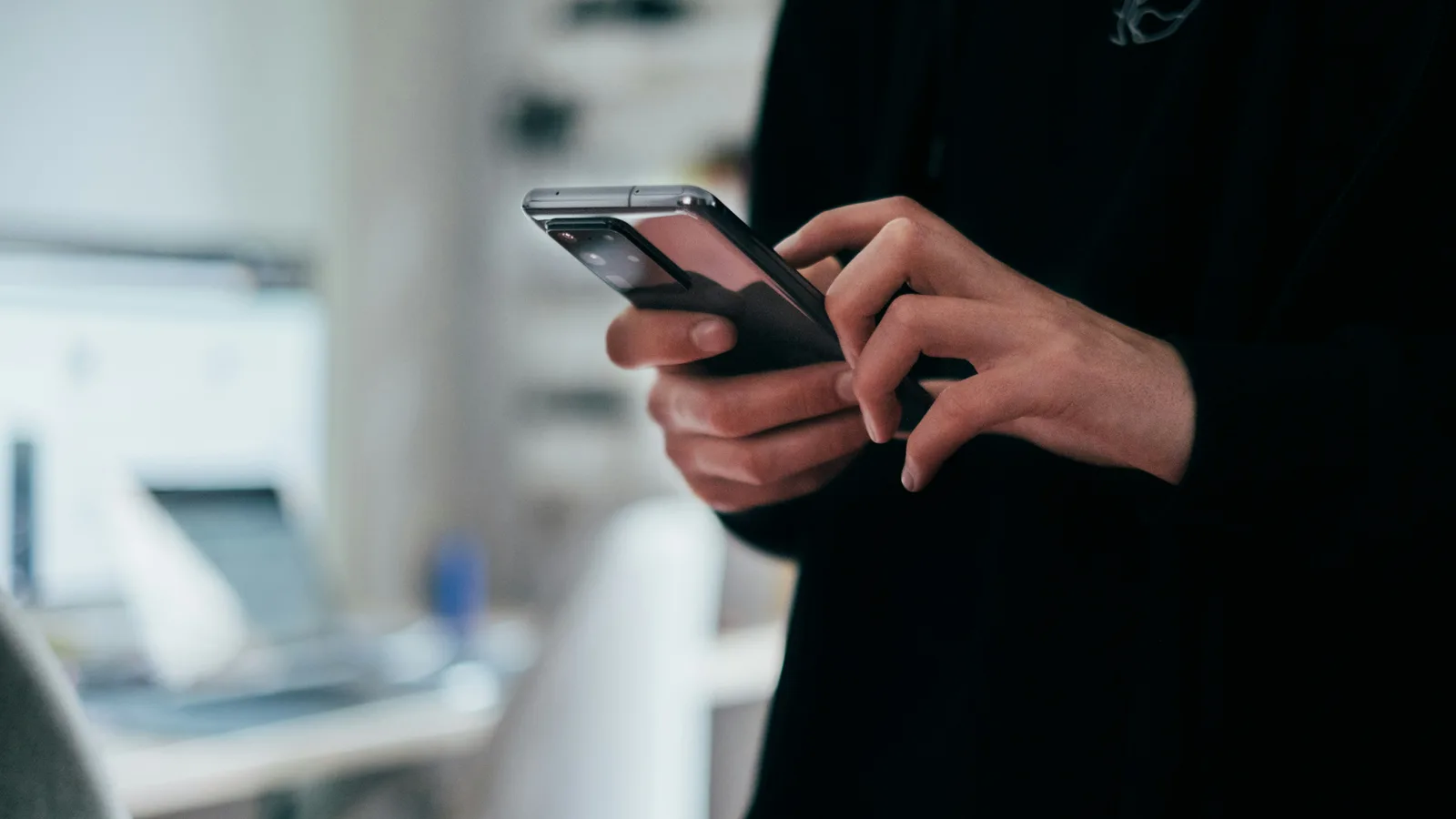 Hands using a smartphone in a bright room.