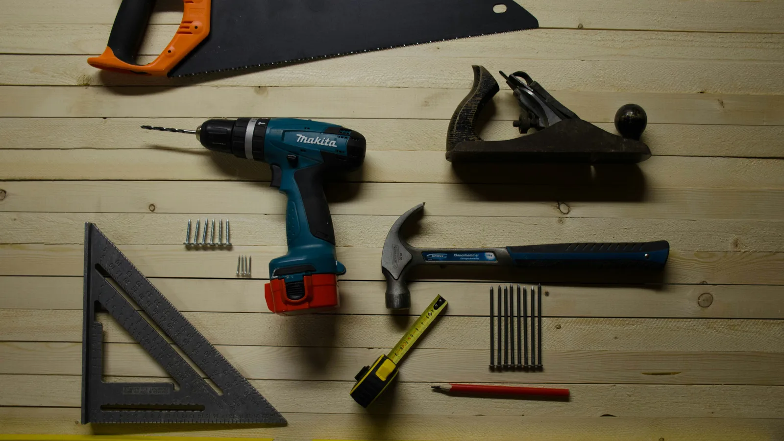Drill, hammer, plane and measuring tools arranged on a wooden surface.