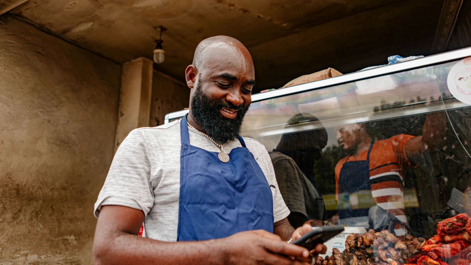 Man wearing an apron and using a smartphone beside a shop display.