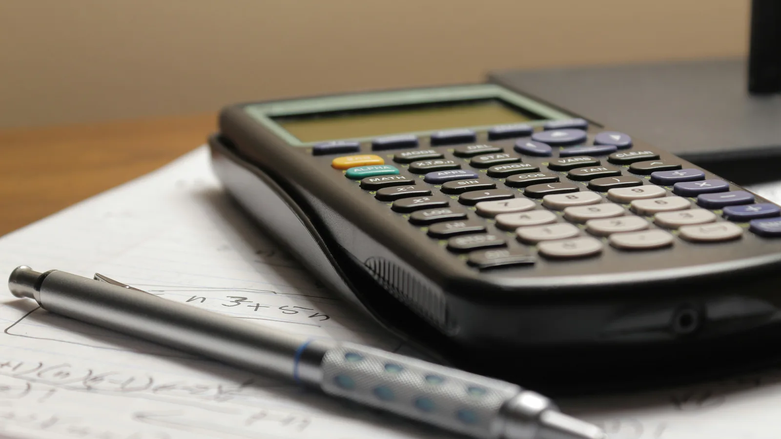 A calculator and a pen sitting on top of a piece of paper.