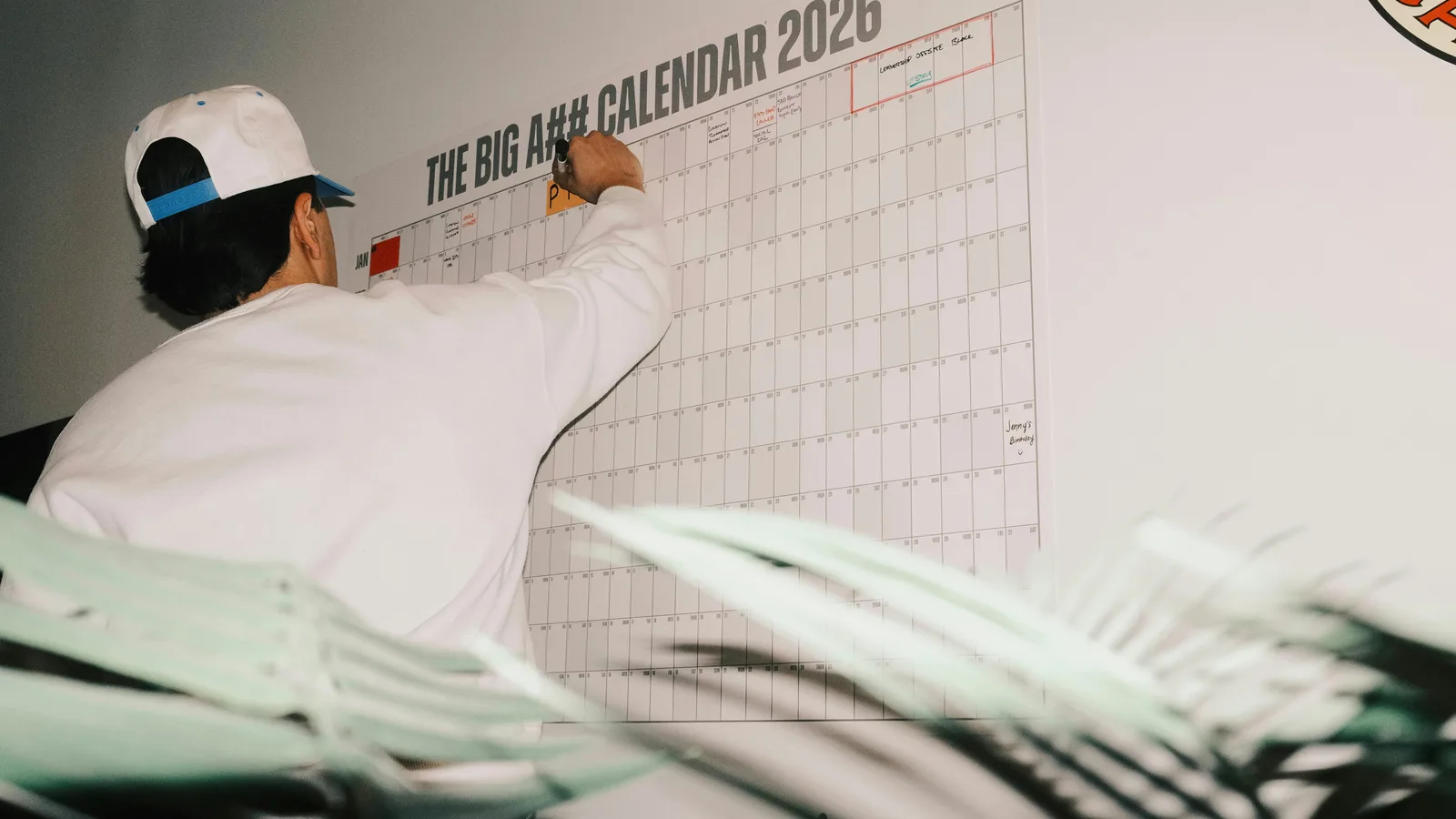 Person marking dates on a large wall calendar.