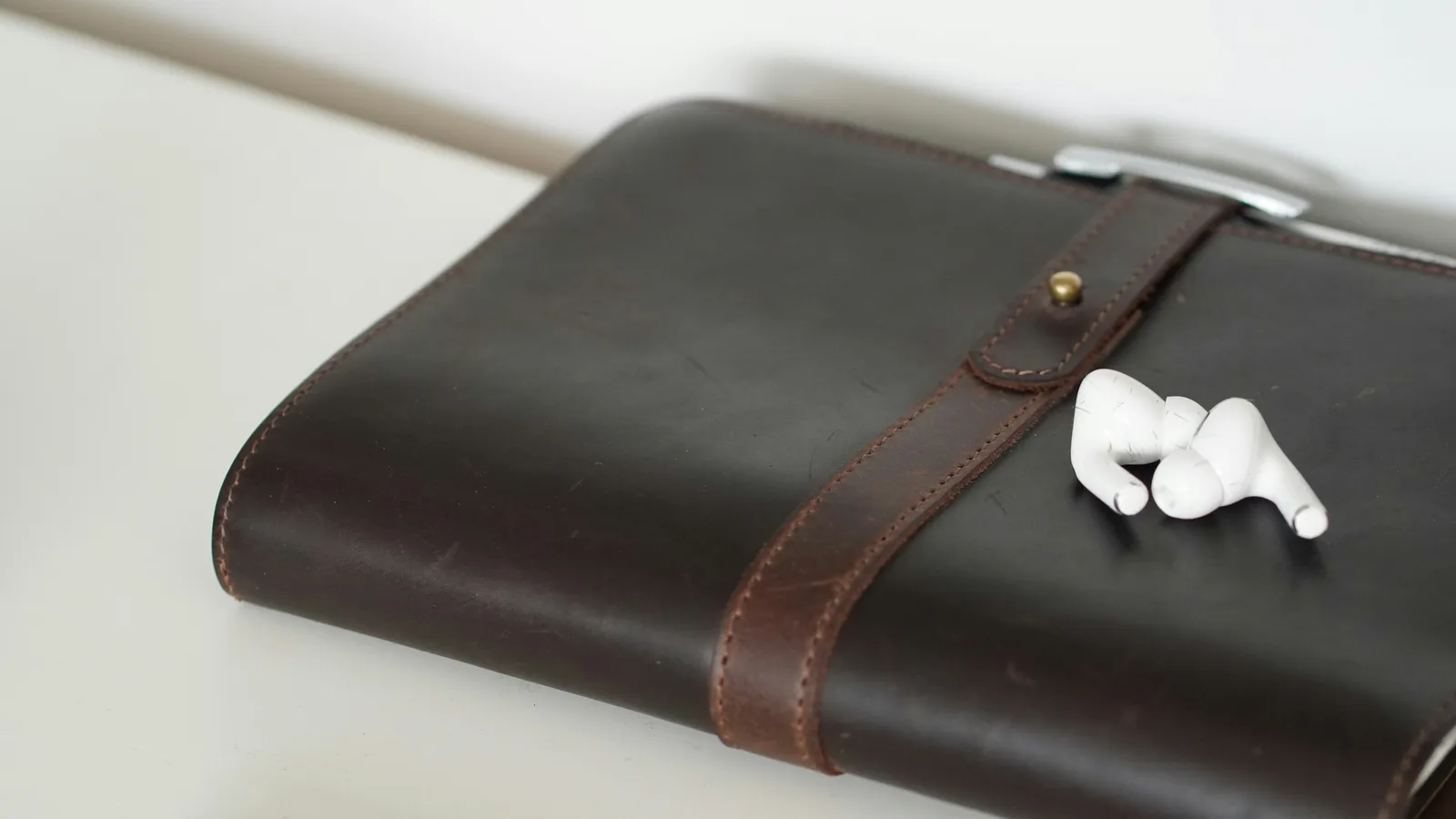 Closed brown notebook with white earbuds on a desk.