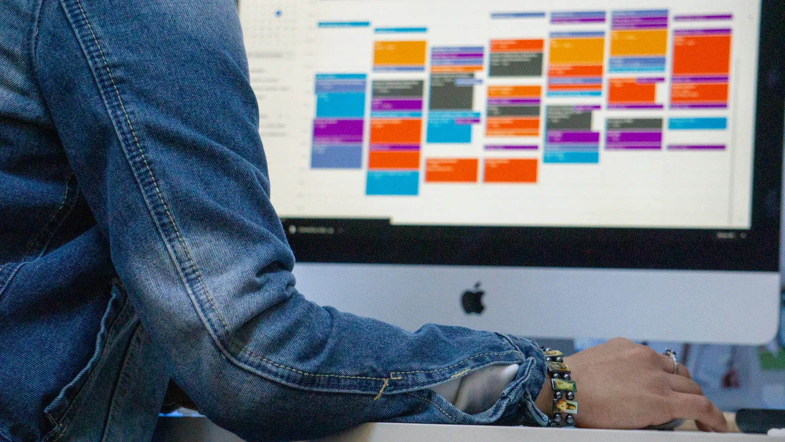 Person using a desktop computer displaying a color-coded calendar.