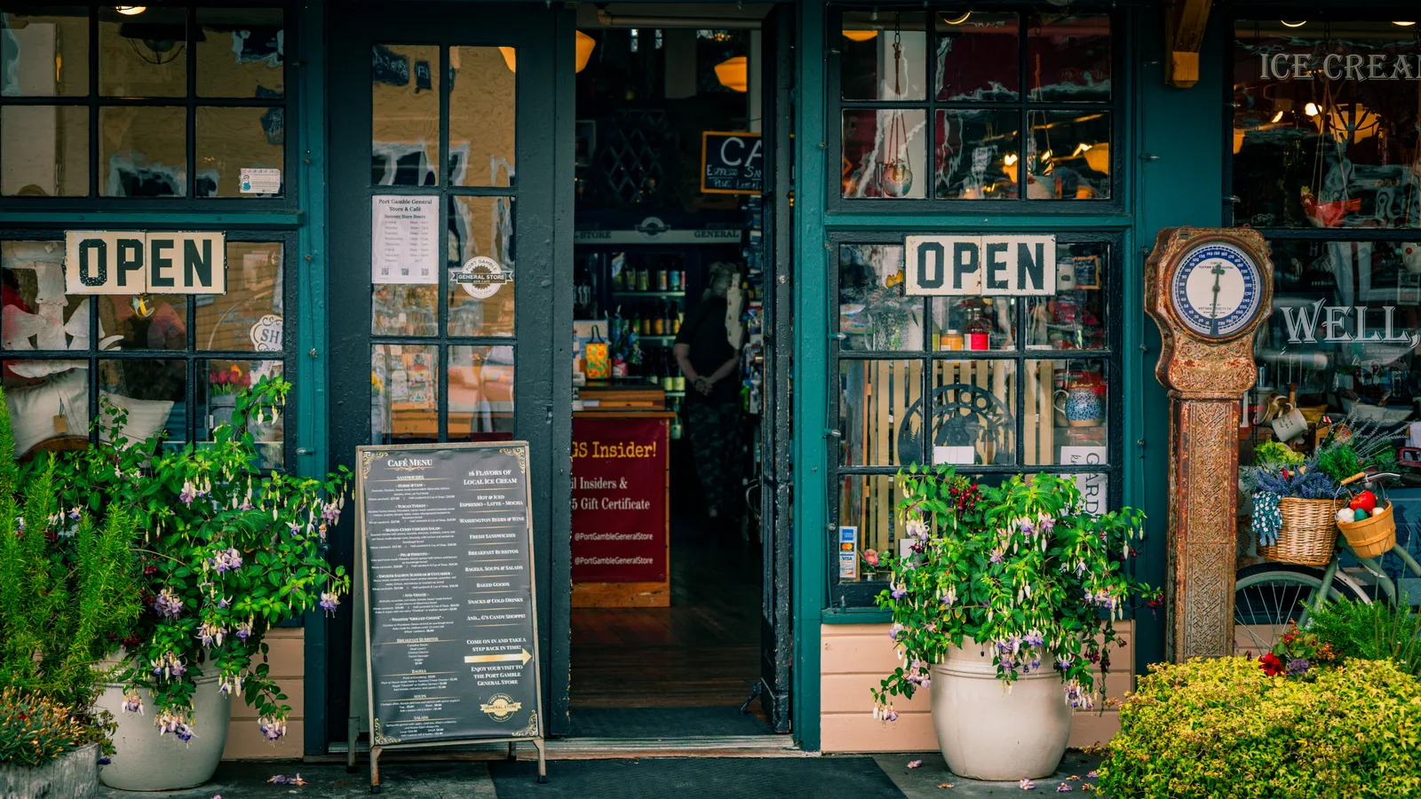 Green storefront with open signs and plants.