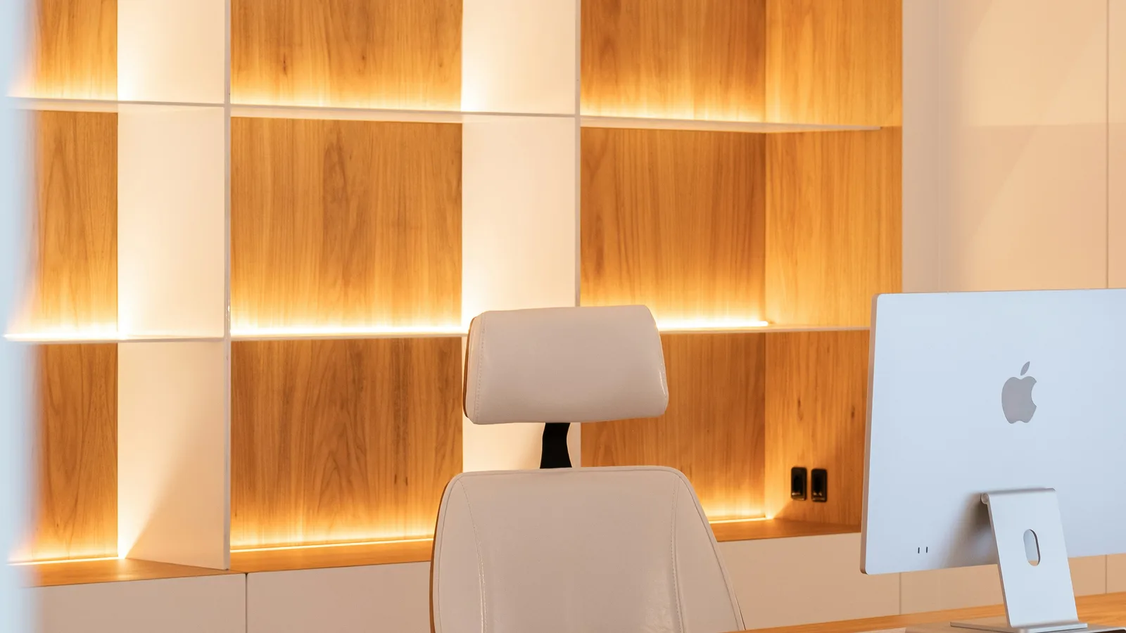 Modern office with wooden desk and illuminated shelves.