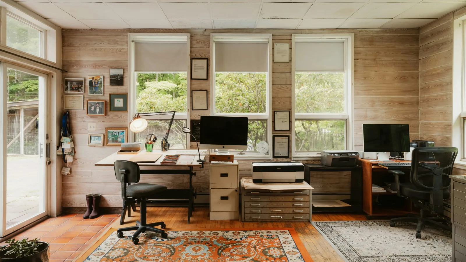 Shared office with two computer workstations beside large windows.