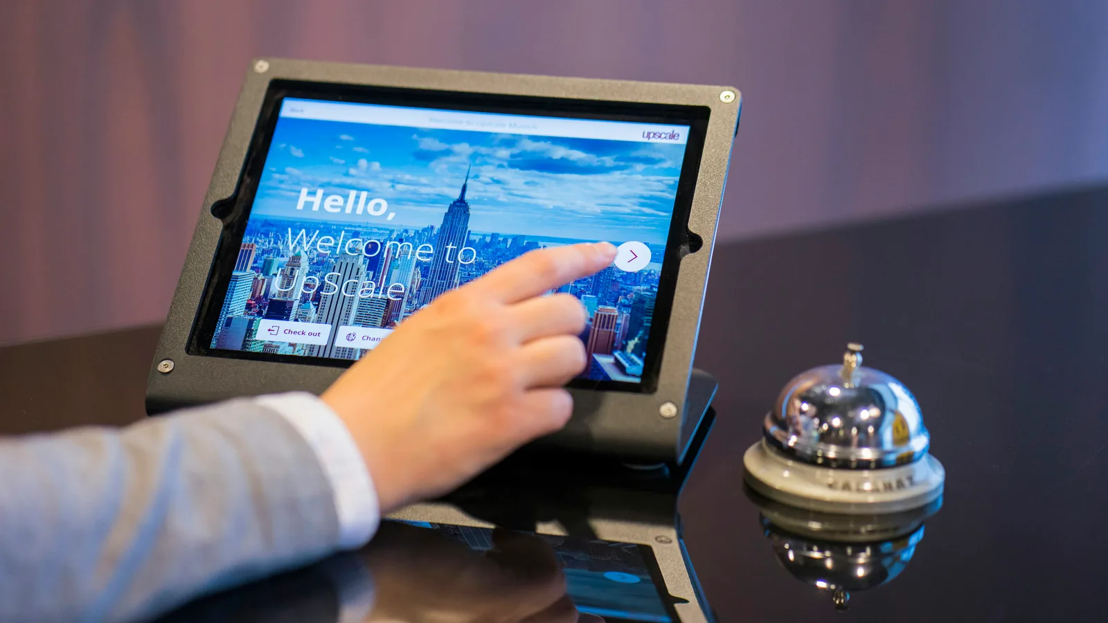 Hand using a tablet at a reception counter beside a service bell.