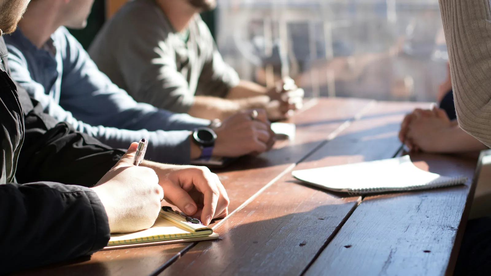 People writing in notebooks during a table discussion.