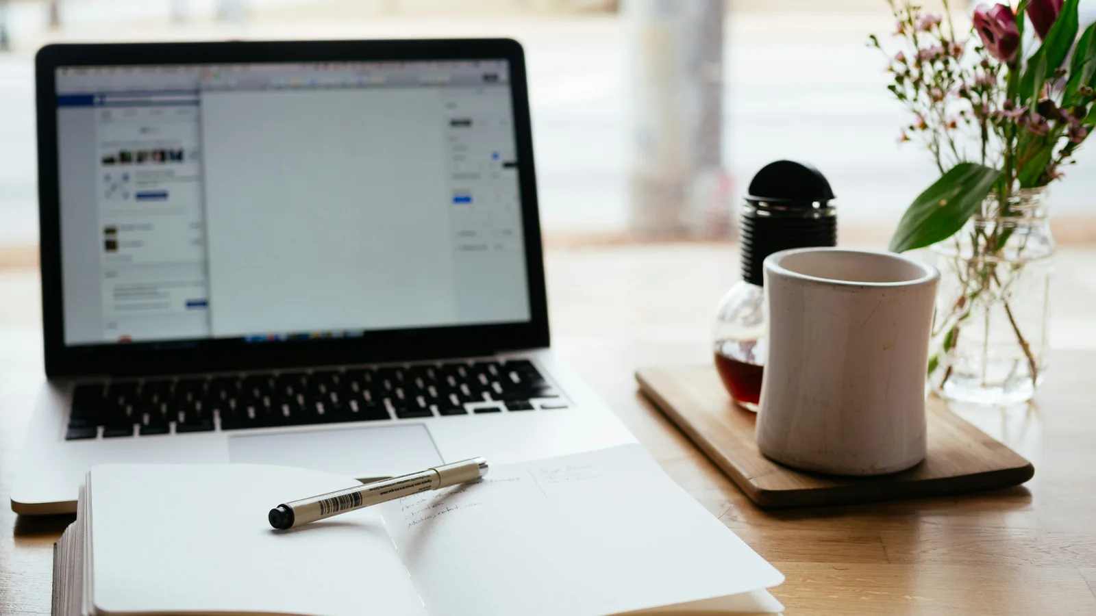 Open laptop, paper, pen and coffee cup on a desk.