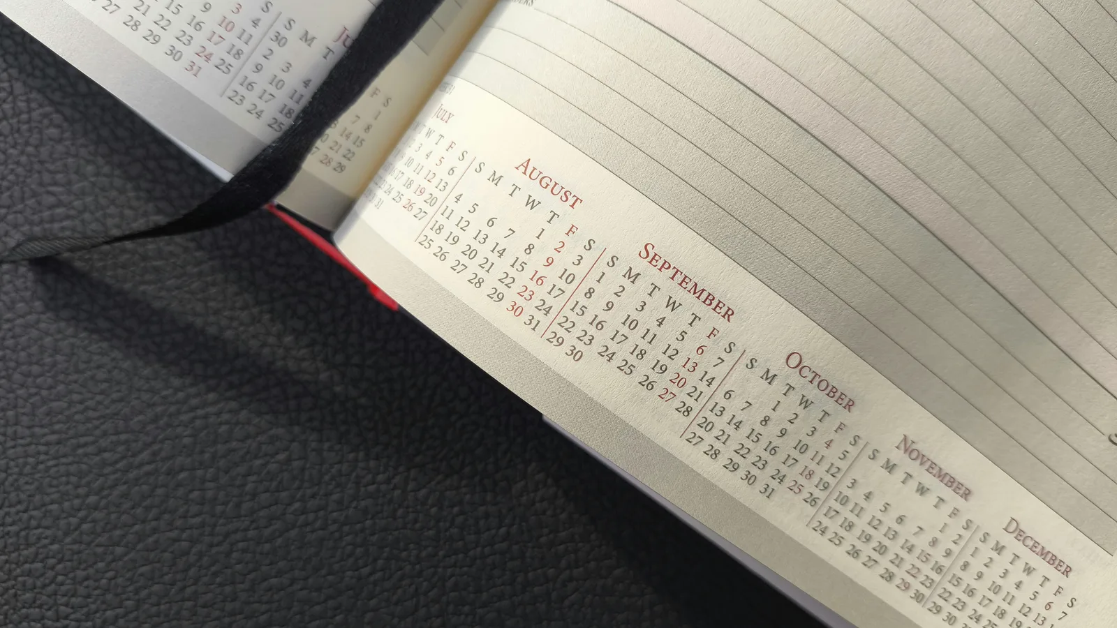 Open notebook with a small printed calendar on a dark surface.